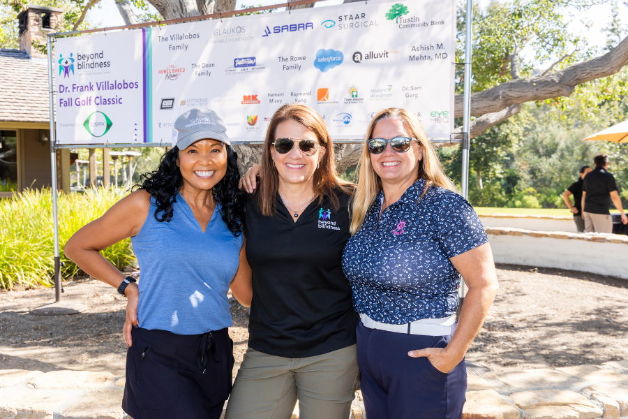 Three woman smiling in front a white sponsor banner