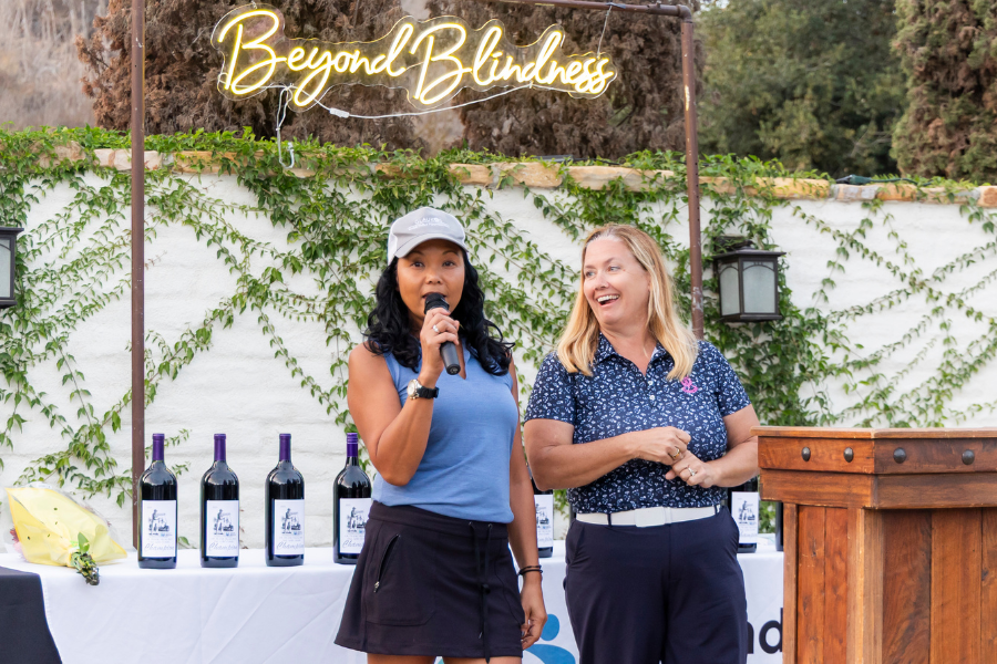 Two women smiling in front of a podium, speaking.