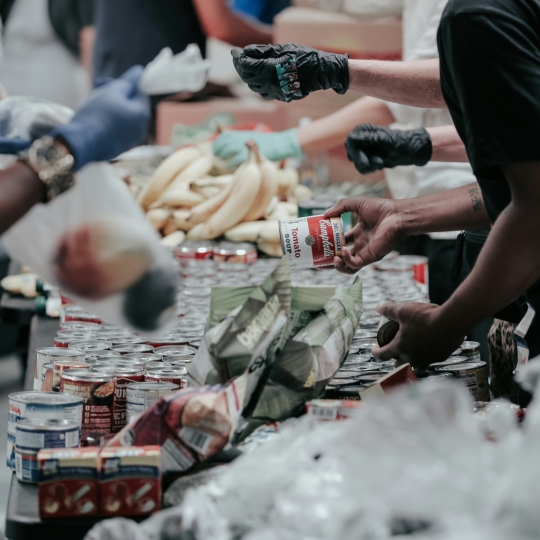 People gathered at a food pantry. Canned food items and bananas are pictures
